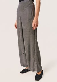 Pantaloni ampi con un motivo geometrico in bianco e nero, caratterizzato da linee e quadrati variabili. Realizzati in un tessuto morbido e testurizzato.