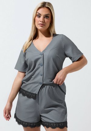 Kvinde iført gråt finstribet knap-op top og matchende shorts med sort blondetrim, stående mod en ensfarvet lys baggrund.