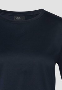 T-shirt noir à col rond avec une étiquette visible S.Oliver Black Label à l'intérieur du col sur un fond clair.