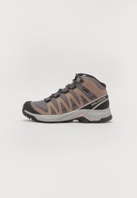 Chaussure de randonnée mi-haute avec une tige en mesh gris et beige, un embout en caoutchouc noir et un talon renforcé. Notable pour son design de panneau latéral complexe.