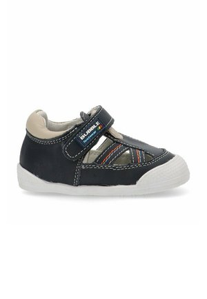 Zapato de cuero negro con acentos beiges, correa de velcro, diseño recortado, suela de goma blanca texturizada y detalles de costura coloridos.