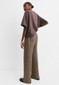 Top corto a maniche corte in cotone viola abbinato a pantaloni larghi in marrone con texture; tessuto liscio per la maglietta, texture sgualcita per i pantaloni.
