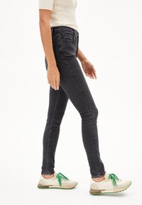 Jean skinny noirs à taille haute, associés à des baskets légères avec des lacets et des accents verts. Texture lisse, design ajusté.
