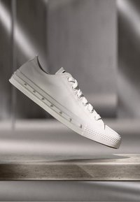 Baskets en toile blanche avec un bout arrondi, semelle en caoutchouc texturée et six œillets pour les lacets. Présente des accents surélevés le long des côtés.