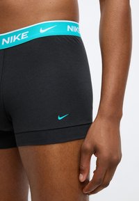 Boxer shorts en coton noir avec une ceinture élastique bleu clair portant le logo "NIKE" et un petit swoosh bleu Nike sur le côté inférieur.