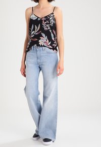 Camisola nera floreale con spalline sottili abbinata a jeans a gamba larga blu chiaro e sneakers bianche. Presenta intricate fantasie di foglie e fiori.