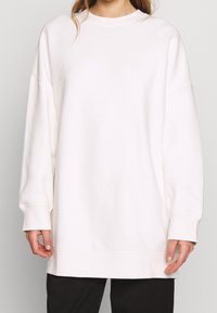 Sudadera blanca de gran tamaño con cuello redondo, hombros caídos, puños acanalados y dobladillo recto. Tela suave con textura lisa.
