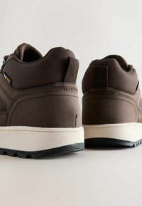 Braune synthetische Sneaker mit einer strukturierten Oberfläche, ausgestattet mit einer weißen Mittelsohle und einer schwarzen Gummisohle. Mit einem Zugriemen an der Ferse.