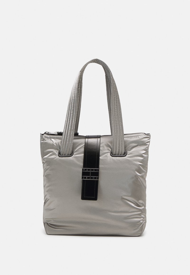 Sac cabas matelassé gris avec double poignées et une sangle verticale noire étiquetée "Tommy Jeans" au centre.
