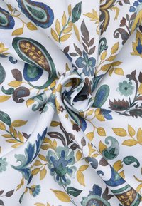 Witte stof met een bloemenpatroon in blauwe, groene en gele elementen, met ingewikkelde bladeren en paisley-vormen. Zachte textuur.