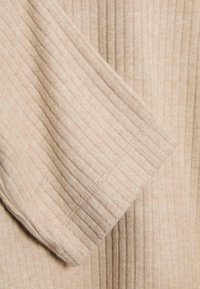 Beige žebrovaná pletenina s jemnou texturou, s vertikálními pruhy a přírodními vlákny, složená tak, aby ukázala vzor a měkkost.