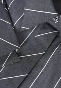 Gros plan d’un tissu gris avec des rayures diagonales blanches et un col pointu avec des coutures visibles et une boutonnière.