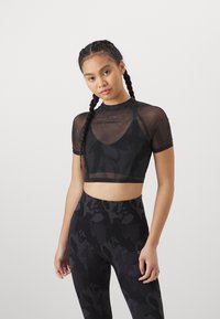 Top de malla negro corto con mangas cortas, con un escote redondo. Combinado con leggings negros de alta cintura con estampado.