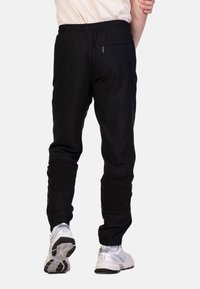 Zwarte joggers met een elastische tailleband, een achterzak met ritssluiting en taps toelopende pijpen, gecombineerd met witte sportschoenen.