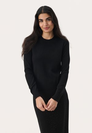 Black knitted sweater with a rounded neckline and long sleeves, made from a soft material. Paired with a black textured skirt with accents.