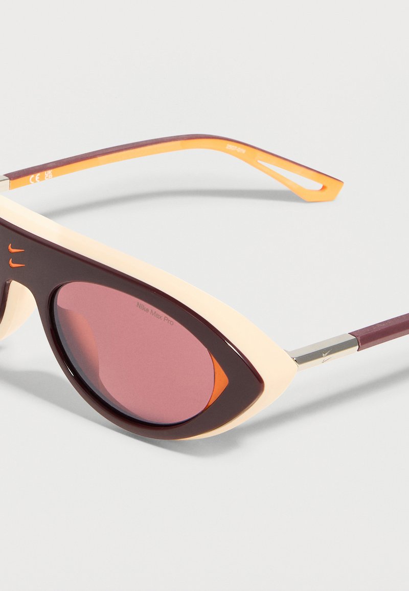 Gafas de sol con forma de ojo de gato, montura en granate y crema, detalles en naranja y lentes tintadas en rosa, de la marca Nike Max Pro.