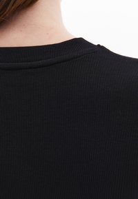 Černá příze s ribovanou strukturou a kulatým výstřihem, která ukazuje jemnou texturu a bezšvový zadní design. Žádné viditelné kovové součásti nebo akcenty.