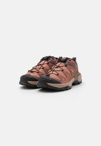 Outdoor shoes with a pinkish-brown textile upper, black accents, reinforced toe, and textured rubber sole for traction.