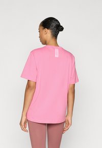 Ružové bavlnené tričko s krátkymi rukávmi a okrúhlym výstrihom, s vertikálnou logo štítkom na zadnej strane. Hladká textúra a ležérny strih.