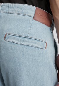 Jasnoniebieskie dżinsy z brązową skórzaną metką z napisem "Marc O'Polo". Posiadają tylną kieszeń z przeszyciem.