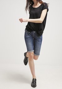 Černý top s krátkým rukávem, modré džínové šortky s ohrnutými lemy a černé nazouvací boty; hladká textura a neformální design.