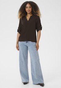 Top noir à manches courtes avec un col en V et des poignets roulés, associé à un jean large bleu clair. L'ensemble présente une coupe décontractée et une texture douce.