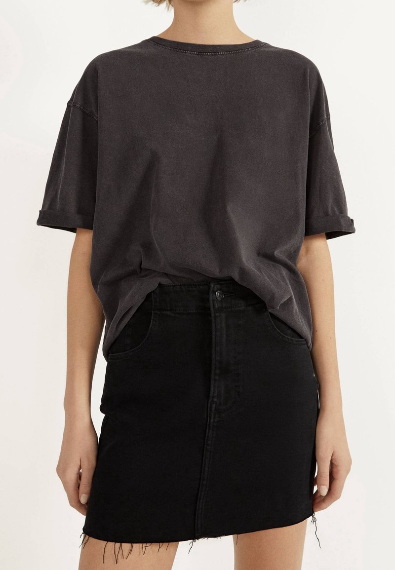 Oversized, donkergrijze katoenen t-shirt met opgerolde mouwen, gecombineerd met een zwarte denimrok met een rafelige onderrand en voorzakken.