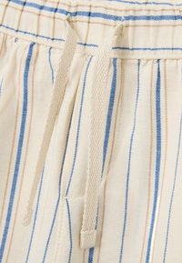 Gros plan sur un tissu rayé avec des lignes crème, bleu et tan. Taille élastique avec cordon pour un ajustement réglable. Texture douce.