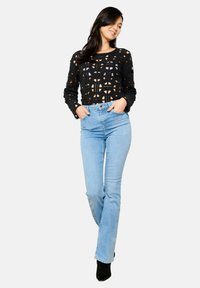 Top de ganchillo negro con diseño abierto combinado con jeans de tiro alto de color azul claro y botas de tobillo negras. Textura de tela plana y forma ajustada.