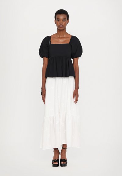 Zwarte top met pofmouwen en vierkante halslijn, gecombineerd met een witte, gelaagde rok met bloemmotief en zwarte platformsandalen.