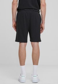Shorts noirs en tissu doux, avec une taille élastique et des poches latérales, se terminant juste au-dessus du genou, associés à des baskets blanches et des chaussettes.