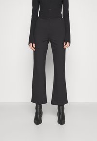 Schwarze, ausgestellte Hosen aus weichem Stoff, mit hohem Bund und glatter Textur, kombiniert mit schlanken, spitzen Stiefeletten.