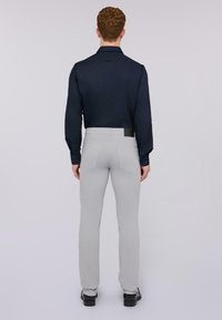 Camicia a maniche lunghe blu scuro abbinata a pantaloni aderenti grigio chiaro, con tasche posteriori e un'etichetta nera in vita. Scarpe flat completano il look.