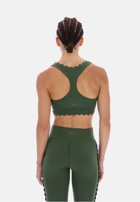 Ciemnozielony sportowy biustonosz z falistymi krawędziami, tyłem typu racerback i detalem z logo. Połączony z dopasowanymi legginsami z wysokim stanem. Gładka faktura.