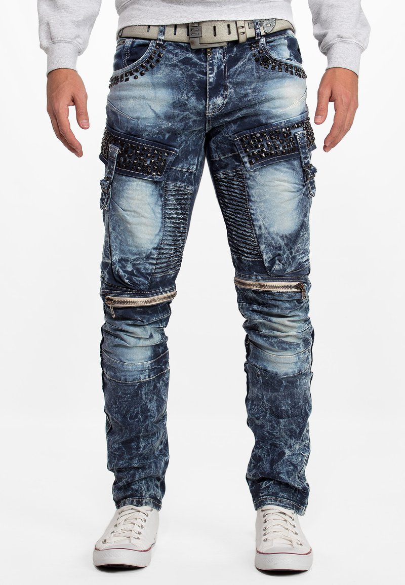 Pantalons cargo en denim bleu clair délavé avec plusieurs poches, détails en zip et rivets métalliques le long de la taille et des poches.