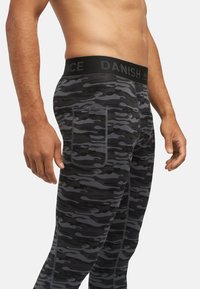 Leggings camouflage noirs et gris avec une texture douce, une taille élastique étiquetée « DANISH » et un détail de poche à l'arrière.