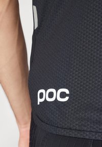 T-shirt de sport noir avec un tissu texturé, présentant un logo "poc" blanc sur le côté et une coupe ajustée. Le design met l'accent sur la fonctionnalité.