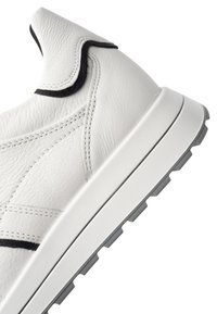 White leather sneaker with black trim, detailed stitching, and a thick white sole with gray tread.