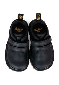 Scarpe di pelle nera con due cinturini in velcro regolabili, punta arrotondata, collo imbottito e un'etichetta gialla pull tab con la scritta "AirWair."