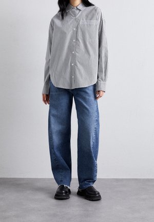 Stribet skjorte med knapper i sort og hvid, kombineret med løse blå jeans med frynset kant, fuldendt med sorte sko.