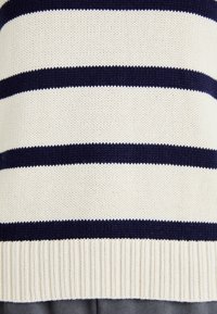 Sweter w paski z kremowymi i granatowymi poziomymi paskami, dzianinowa tekstura, ściągacz u dołu oraz miękki, średniej wagi materiał.