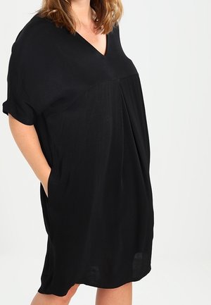 Černé šaty s krátkým rukávem a výstřihem do V, volného střihu a postranními kapsami. Vyrobené z měkké, lehké látky s jemným pádem a texturou.