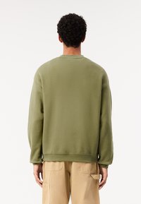 Felpa verde oliva con maniche lunghe, polsini a coste e girocollo. Tessuto morbido con una vestibilità rilassata, abbinata a pantaloni cargo beige.