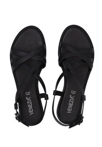 Schwarze Sandalen mit gekreuzten Riemen, aus Leder gefertigt. Sie verfügen über eine flache Sohle und einen Knöchelriemen mit Schnalle. Logo auf der Innensohle gedruckt. Glatte Textur.