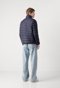 Navy puffer jacket with a standing collar and horizontal quilted design, paired with light blue wide-leg jeans and beige shoes.