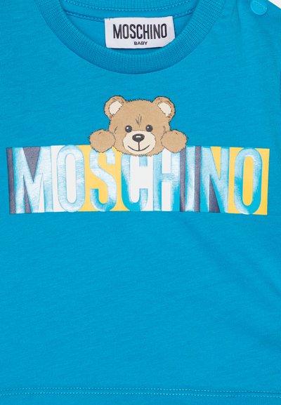 Türkises T-Shirt mit einem Bärenmotiv und dem Text "MOSCHINO" in verschiedenen Farben. Hergestellt aus weicher Baumwolle mit Druckknopfverschlüssen an der Schulter.