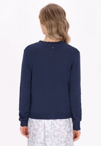 Navy blue knitted sweater with long sleeves and a scalloped neckline. Features a label on the back, textured fabric, and ribbed cuffs.