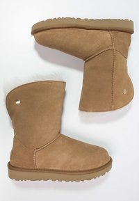 Bottes cheville en daim marron clair avec un manchon en fourrure douce, dotées d'une couture latérale surpiquée et d'une semelle en caoutchouc plate. Bouton décoratif en métal sur le côté.