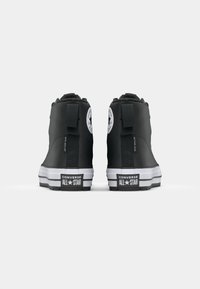Schwarze High-Top-Sneaker mit Gummisohle, versehen mit einem weißen Logo auf der Ferse und einem strukturierten Obermaterial. Enthält Zugschlaufen für ein einfaches Anziehen.