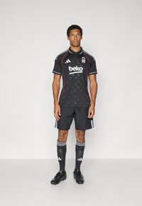 Juoda futbolo apranga su geometriniu raštu, baltais akcentais ir apykakle. Įeina šortai ir dryžuotos kojinės. Juodi batai.